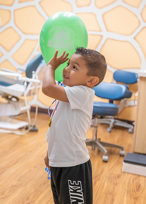 Young boy holding a green balloon in Morgan Hill dental office