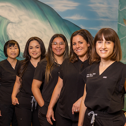 Five smiling dental team members in black scrubs