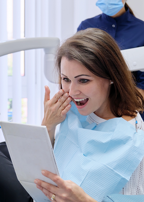 Dental patient looking at her smile in a mirror after cosmetic dentistry in Morgan Hill