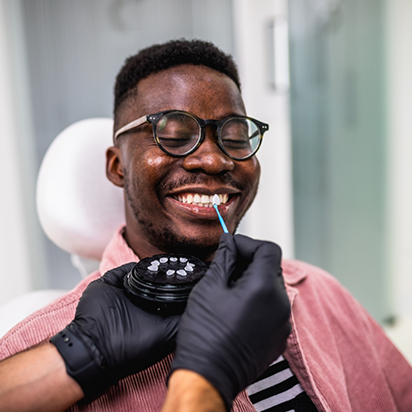 Cosmetic dentist holding a veneer to a smiling patients teeth