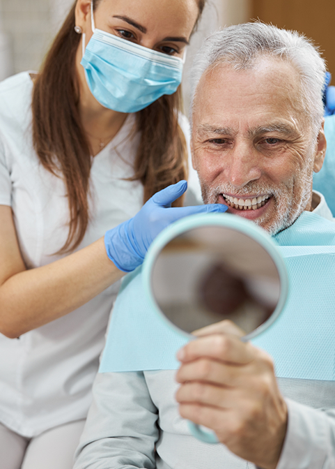 Senior dental patient looking in the mirror at his new smile with dentures in Morgan Hill