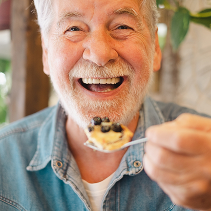 Senior man smiling while holding a spoonful of food