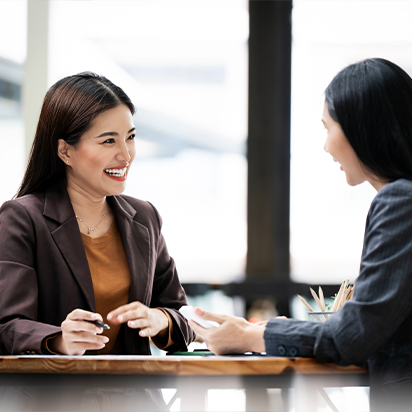 Two women in professional attire sitting across a desk and smiling at each other