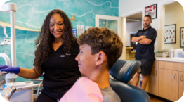 Dental patient sitting in treatment chair and talking to dental team member