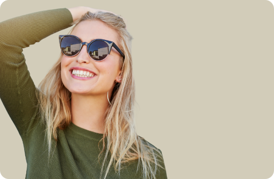 Smiling blonde woman in sunglasses pushing her hair back