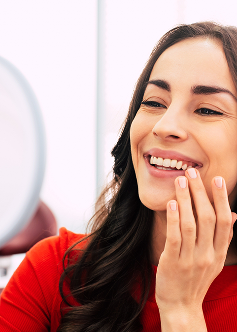 Woman admiring her smile in a mirror after replacing missing teeth in Morgan Hill