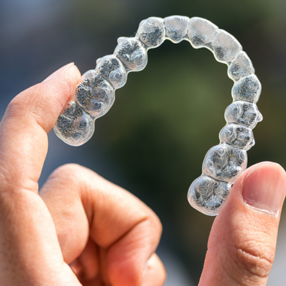 Close up of a hand holding an Invisalign clear aligner