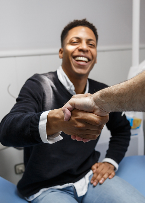 Smiling man in dental chair shaking hands with his dentist